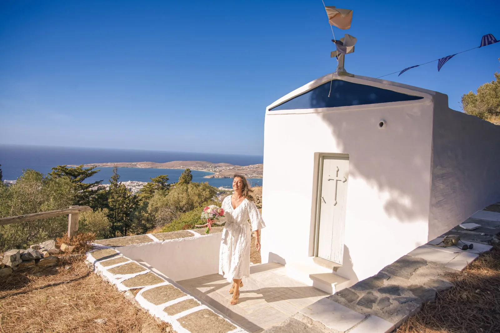 destination-engagement-photography-greece-bride-walking-toward-white-hilltop-chapel-in-paros